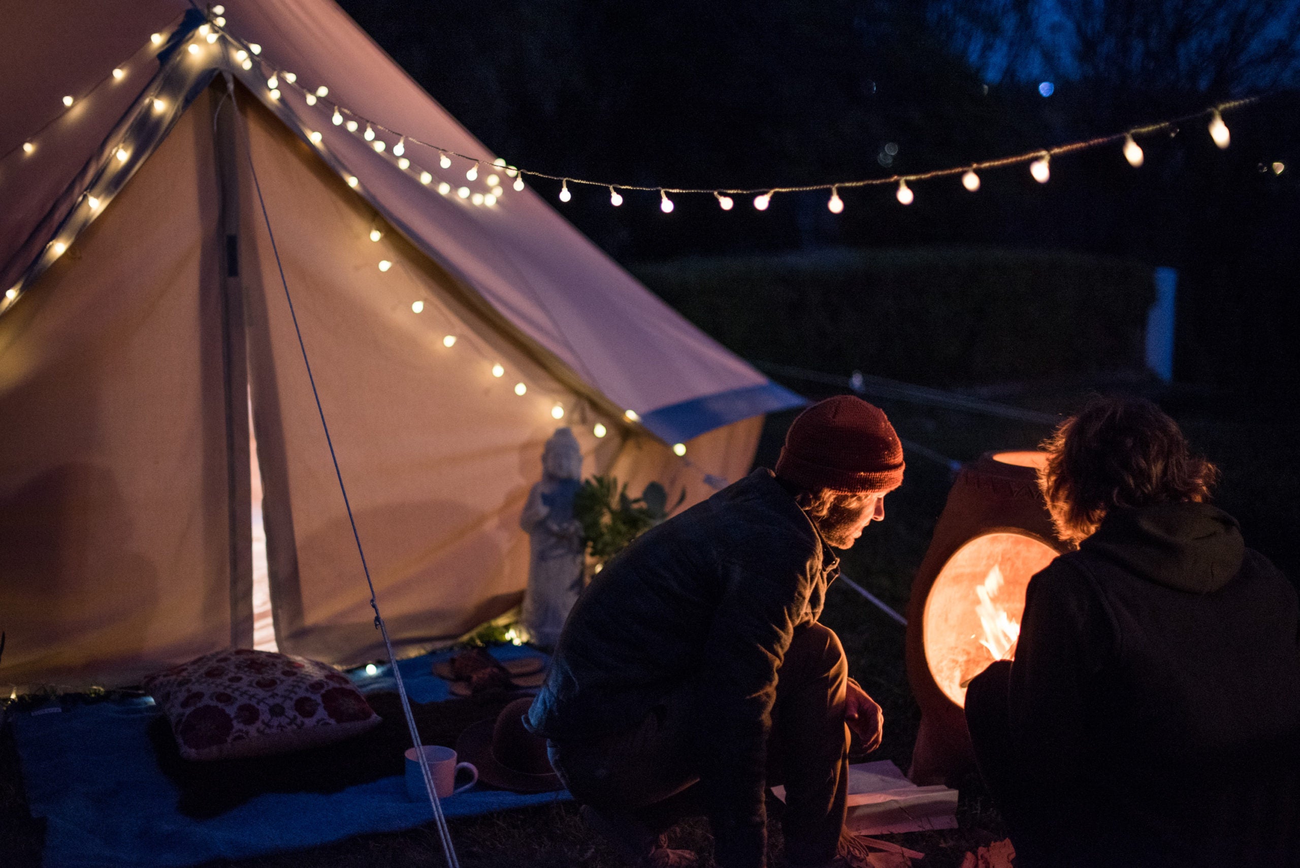 Two men check the fire in front of their canvas Stout Tent Stargazer bell tent
