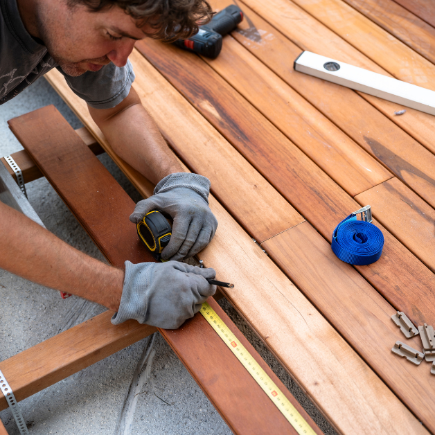 Neatly organized stacks of pressure-treated lumber, concrete deck blocks, and heavy-duty exterior deck screws on grass.