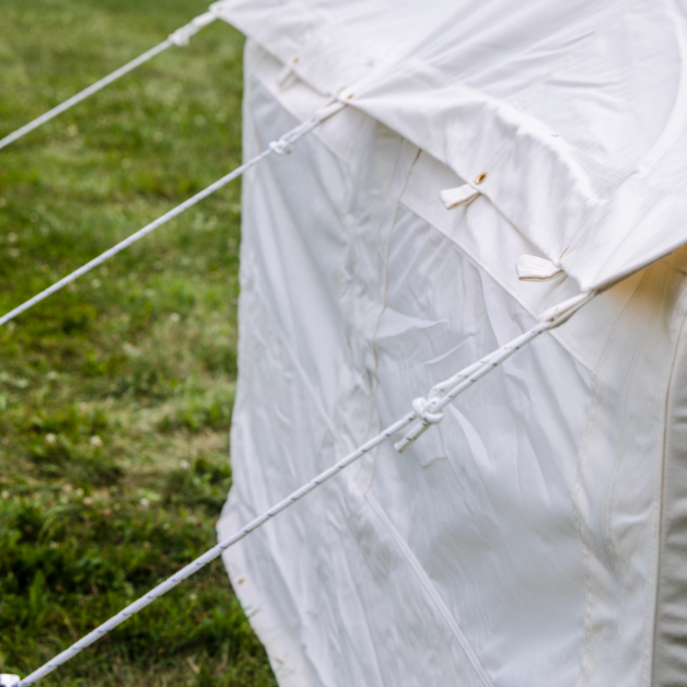 Wall of a white tent with ropes on a grassy background