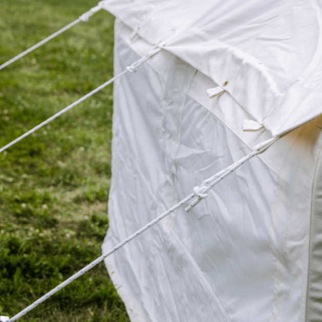 Wall of a white tent with ropes on a grassy background