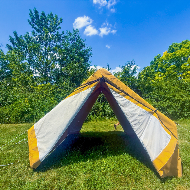 Beige and white wall tent set up in a grassy area with trees in the background