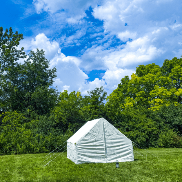 White wall tent in a grassy area with trees and blue sky