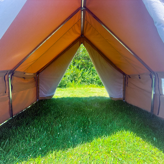 Interior of beige wall tent with grass floor and trees in the background