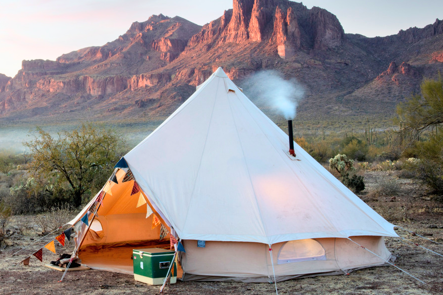 Camping scene with a tent and stove in the desert at sunset.