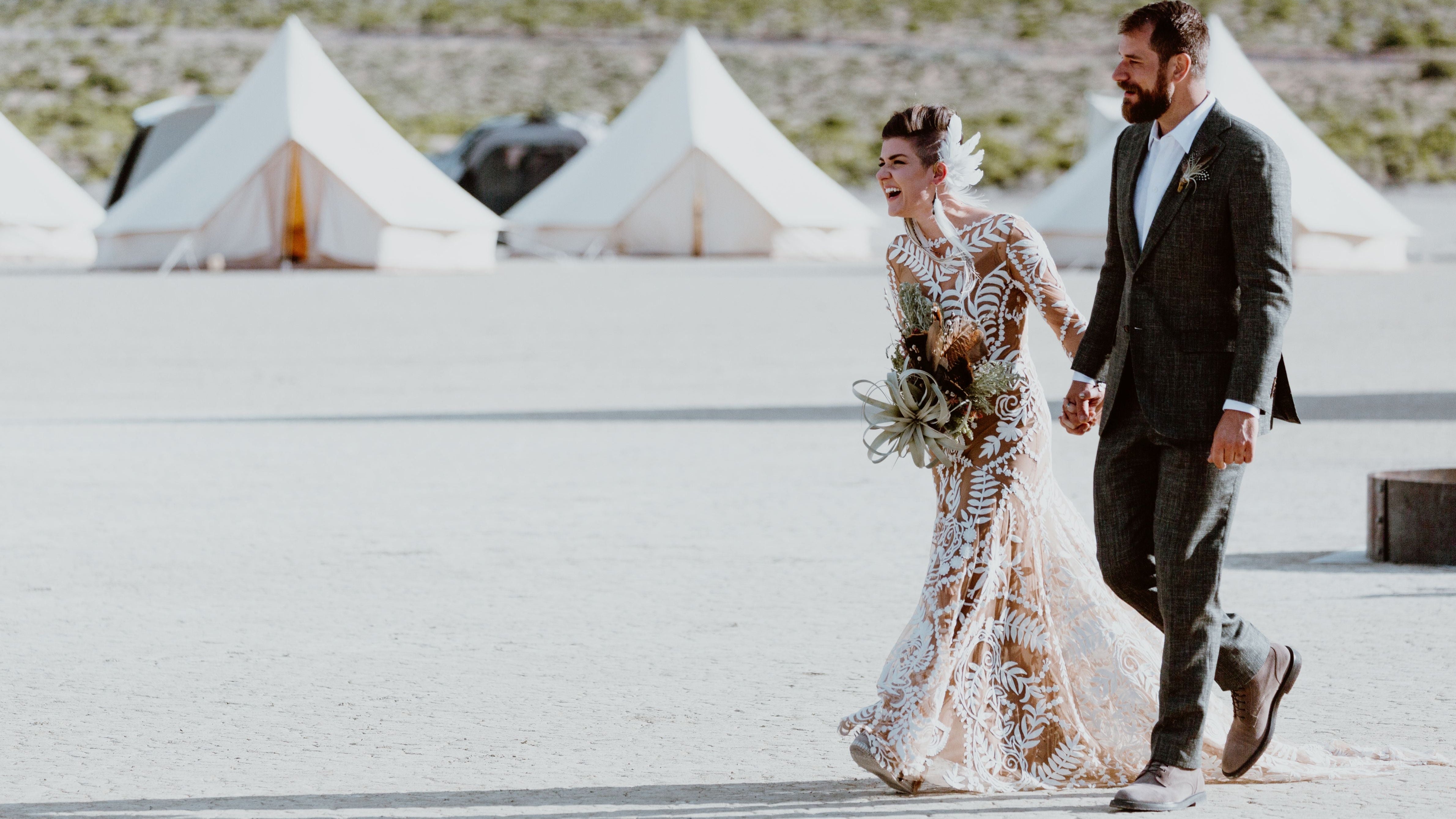 Couple walking together with desert scenery and tents in the background
