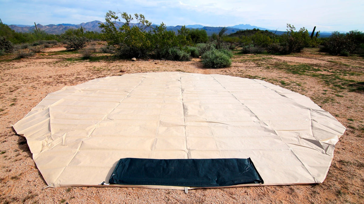 Large beige tent footprint on the ground with a rectangular black section in a desert landscape.