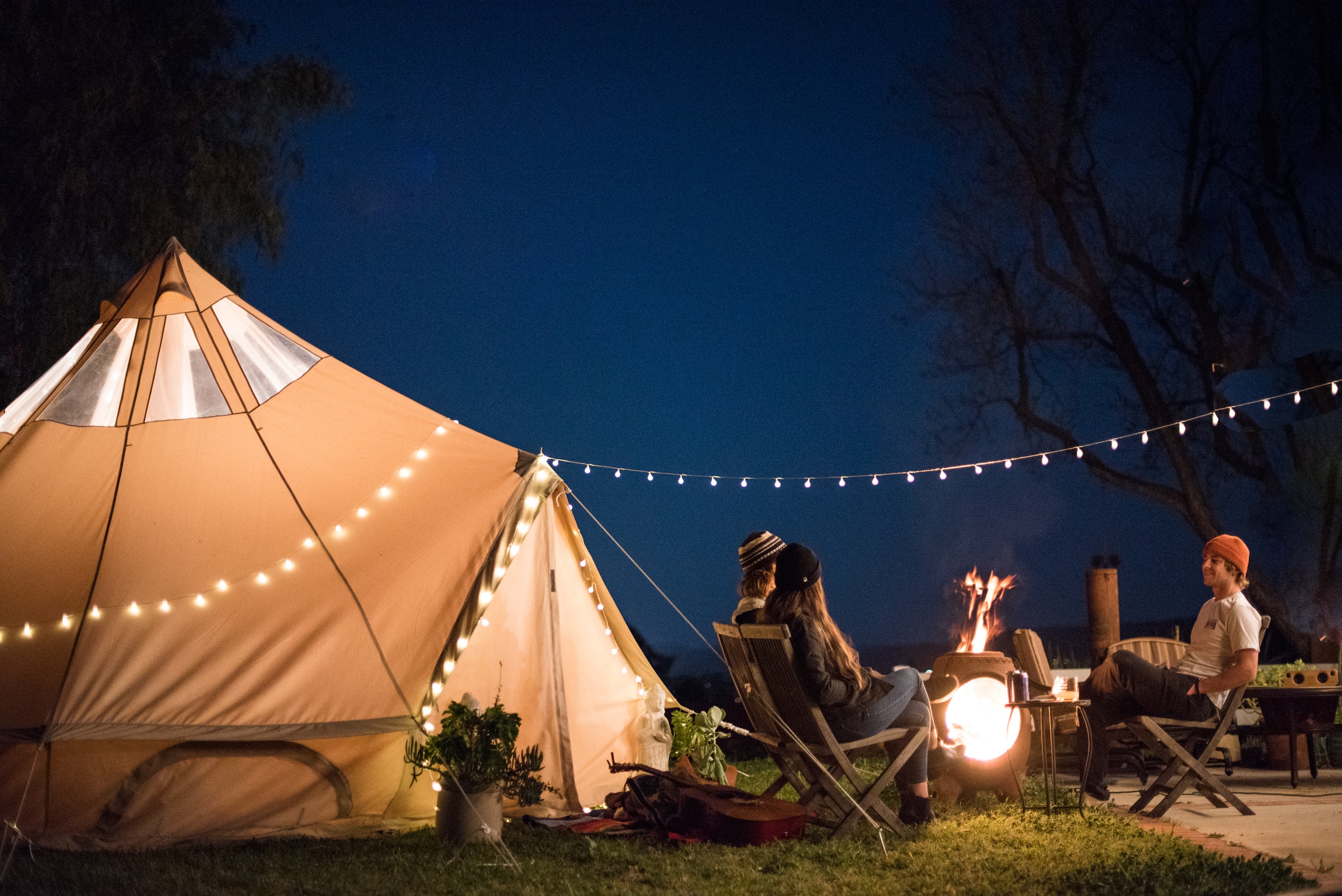 People sitting by a tent with string lights at night
