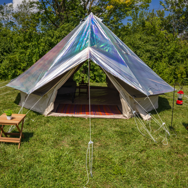 Holographic tent set up outdoors with a table and lantern in a grassy area with trees.