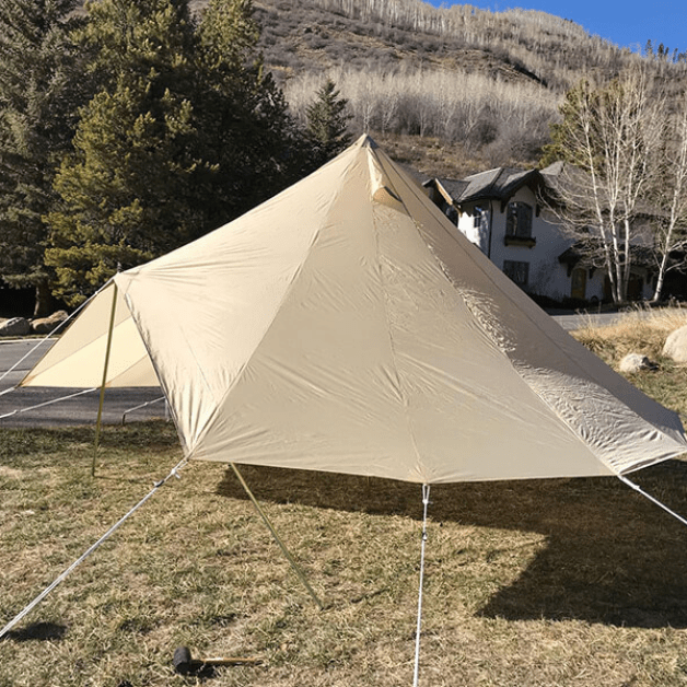 Beige rainfly set up alone outdoors with trees and a building in the background