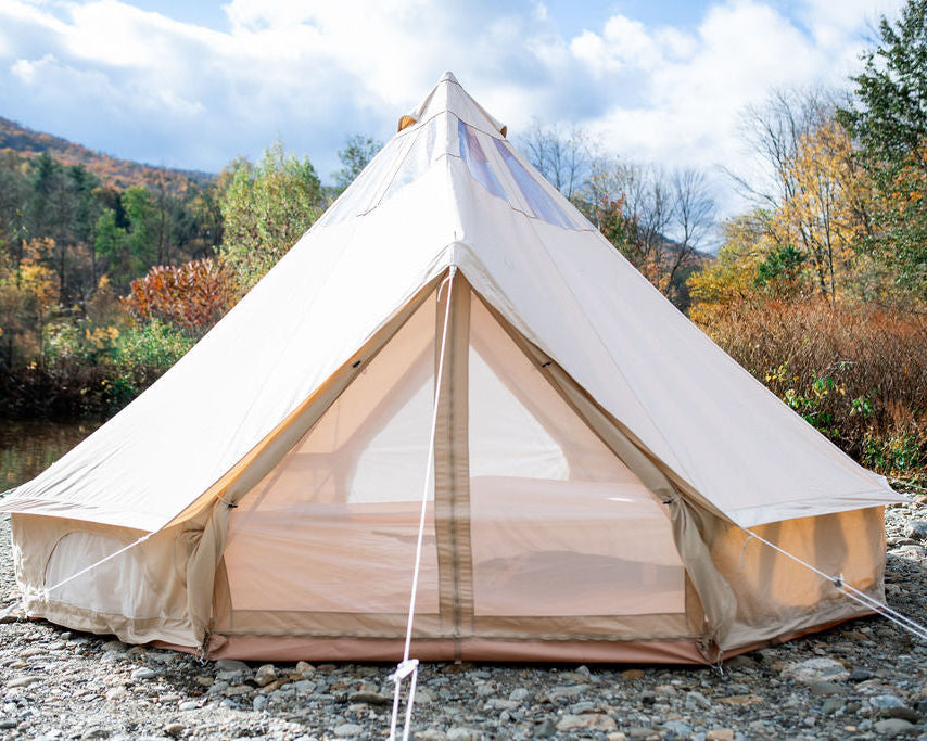 Beige bell tent set up outdoors with a natural landscape in the background