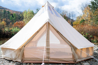 Beige bell tent set up outdoors with a natural landscape in the background