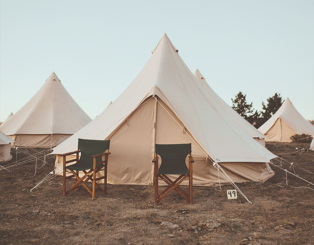 Beige bell tents with green chairs on a grassy field