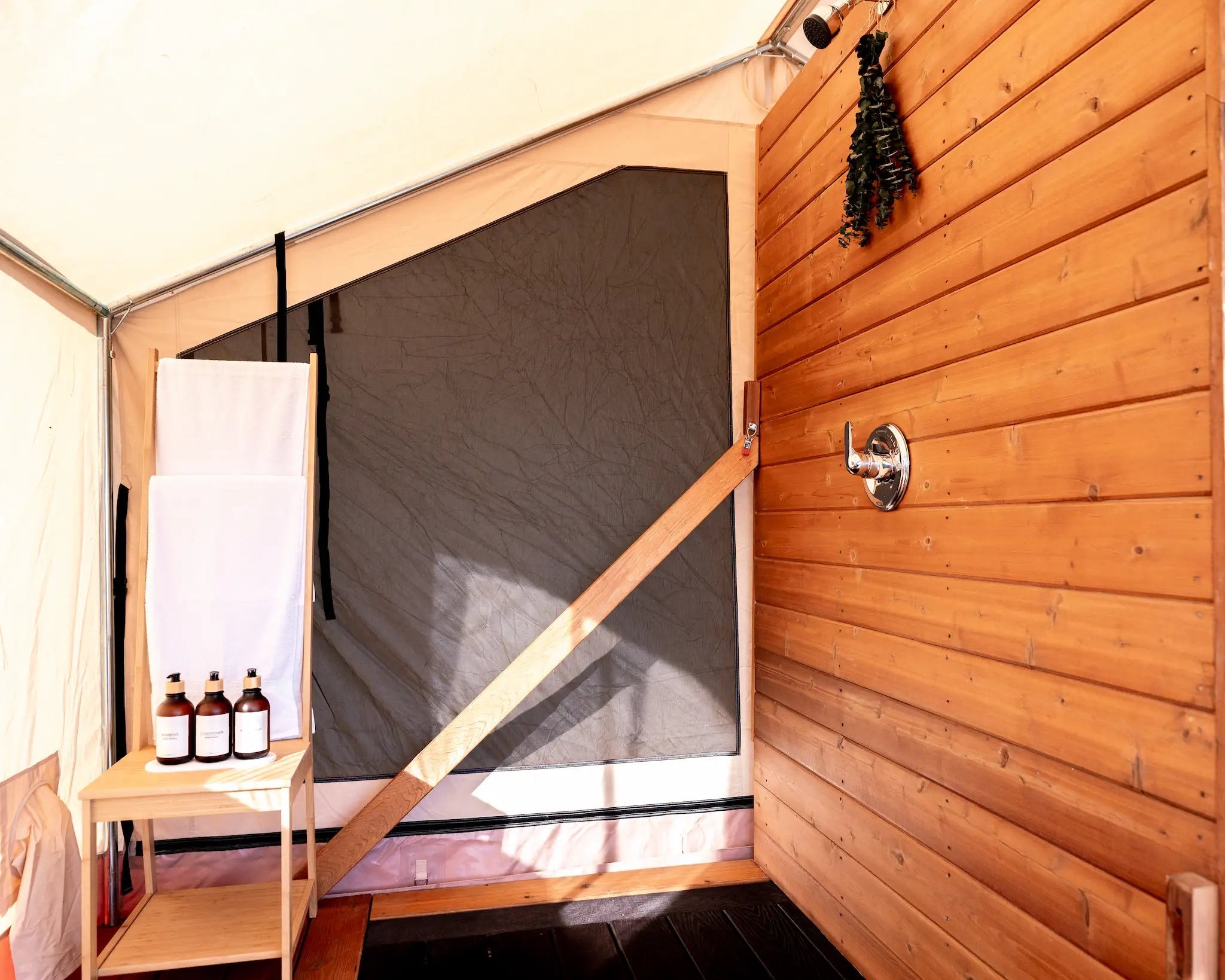 Wooden shower cabin with a screen door and towels hanging inside.
