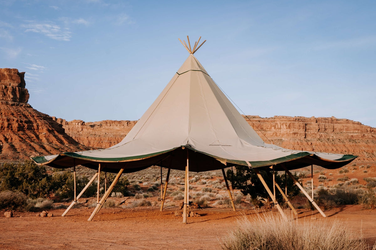 Tipi-style tent in a desert landscape with rocky formations and clear sky