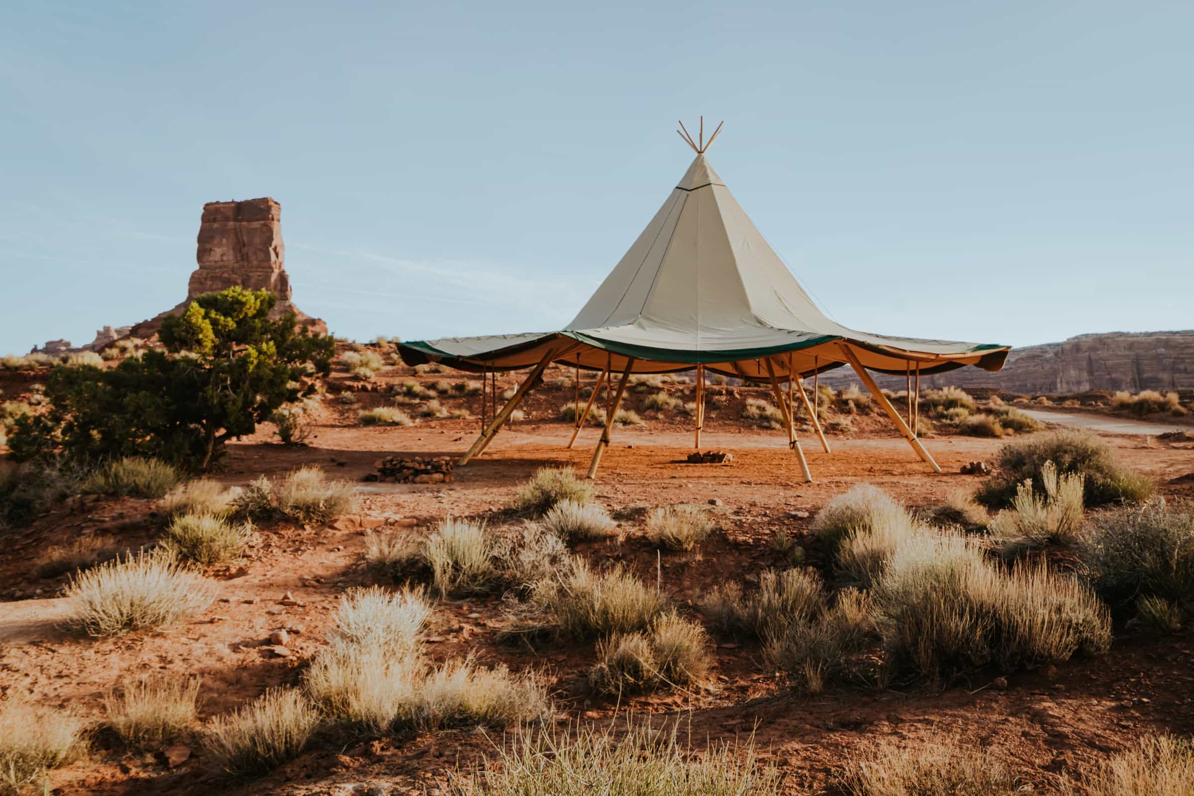 Teepee-style tent in a desert landscape with rocky formations and sparse vegetation.