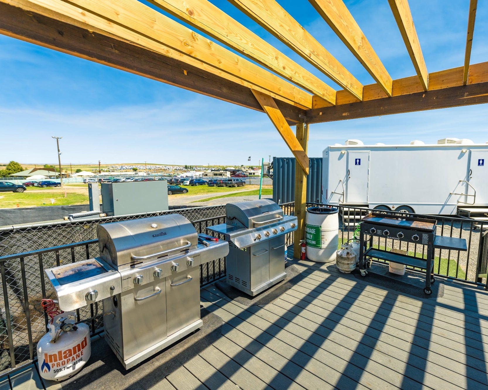 Outdoor grilling area with stainless steel grills under a wooden pergola.