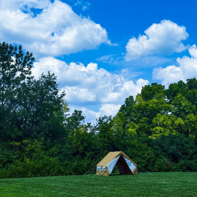 Beige wall tent in a grassy field with trees and a blue sky