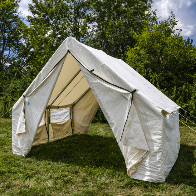Beige and white wall tent set up outdoors with trees in the background