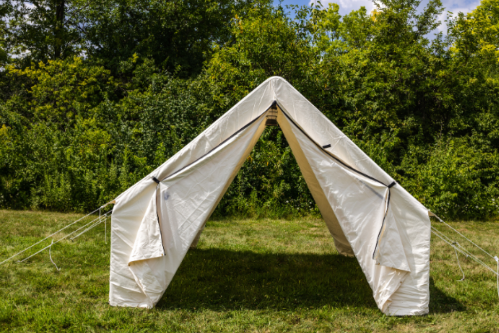 White wall tent set up in a grassy area with trees and blue sky in the background