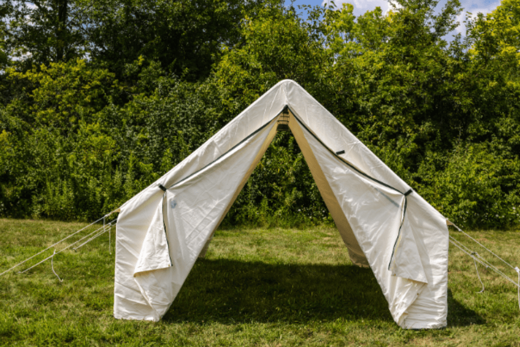 White wall tent set up in a grassy area with trees and blue sky in the background