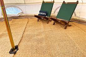 Two green deck chairs with wooden frames on a beige textured rug inside a tent.