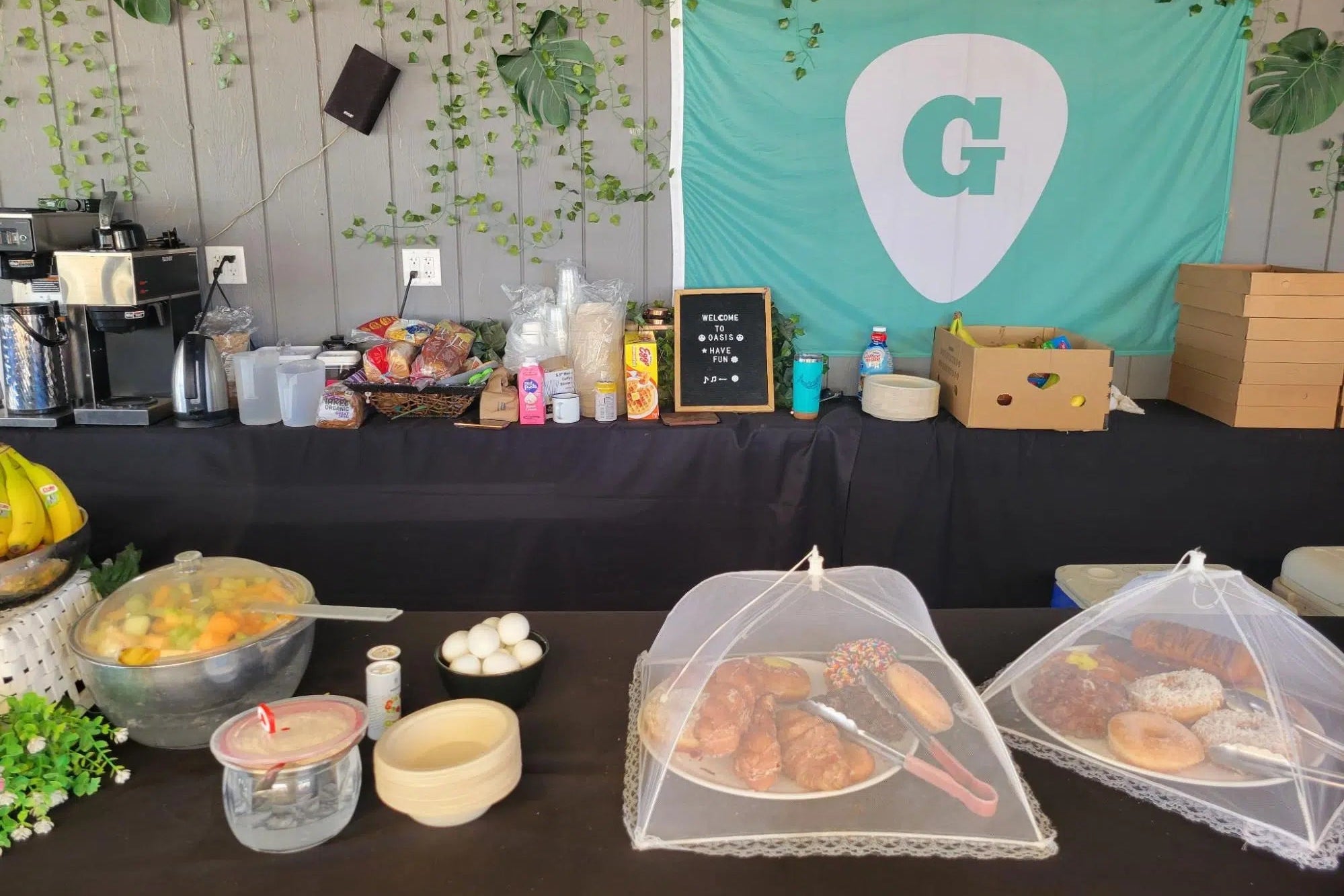 Buffet setup with food items on a table, decorated with a teal banner featuring a logo.