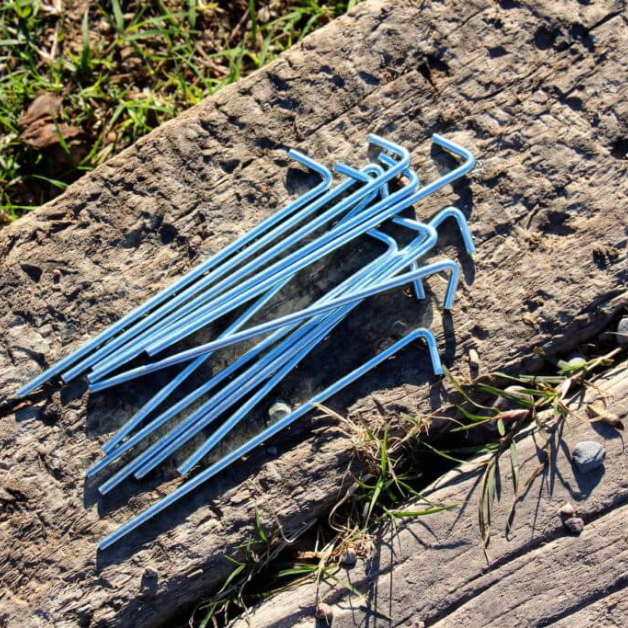 Silver tent stakes on a wooden surface with grass in the background
