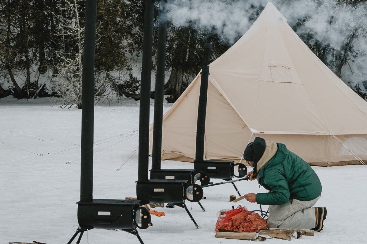Person camping in a snowy landscape with a tent and portable stove.
