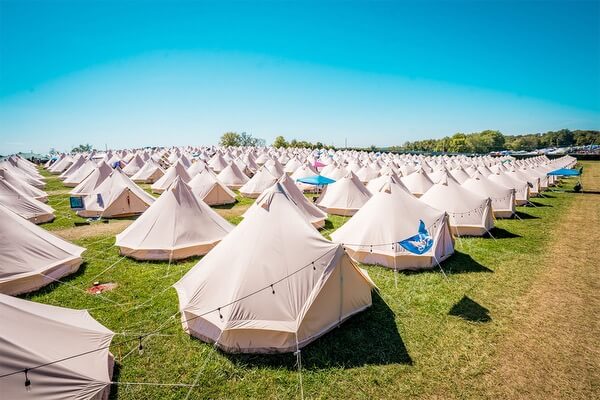 A large-scale festival glamping village featuring a fleet of white Stout Bell Tents set up in a professional grid for event lodging.