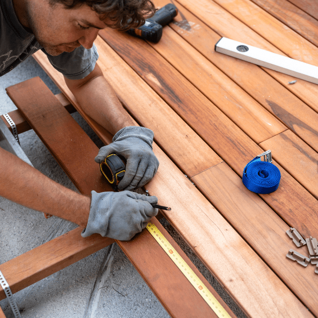 Neatly organized stacks of pressure-treated lumber, concrete deck blocks, and heavy-duty exterior deck screws on grass.