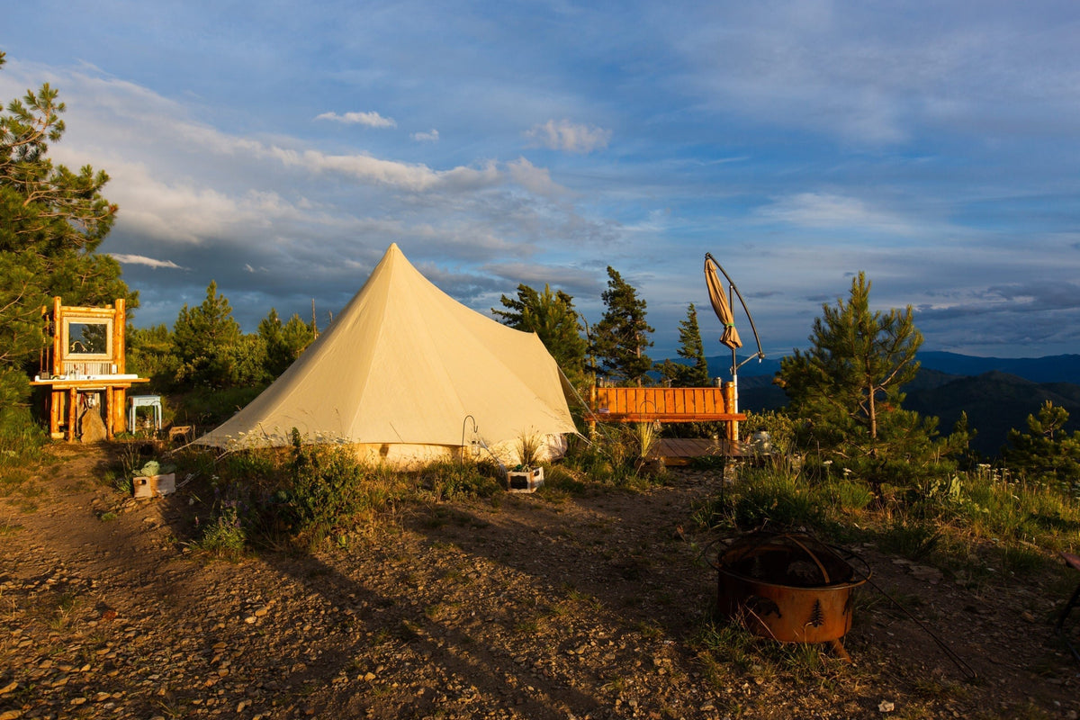 A professional canvas bell tent set up on a modular wooden platform in a scenic mountain glamping site.
