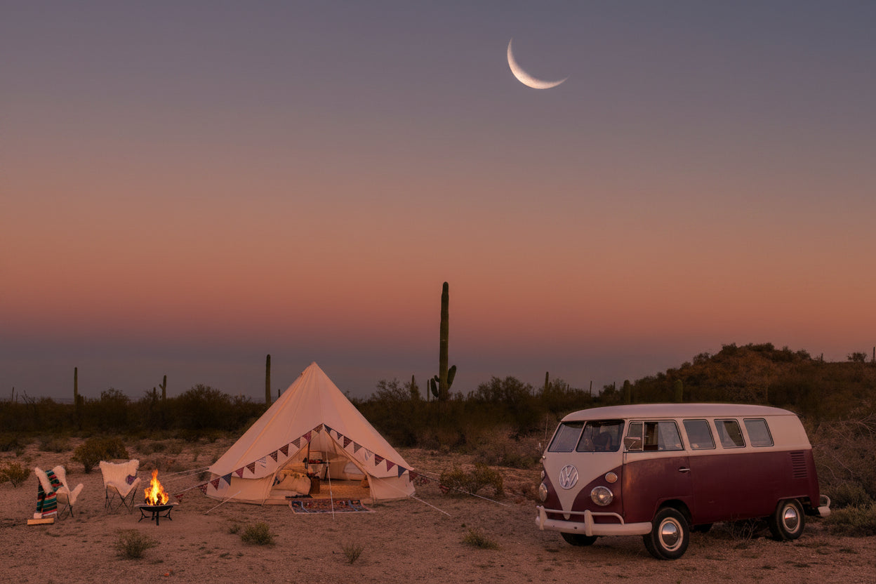 A Stout Tent bell tent and a vintage camper van set up in the desert at twilight, with a campfire burning nearby under a crescent moon