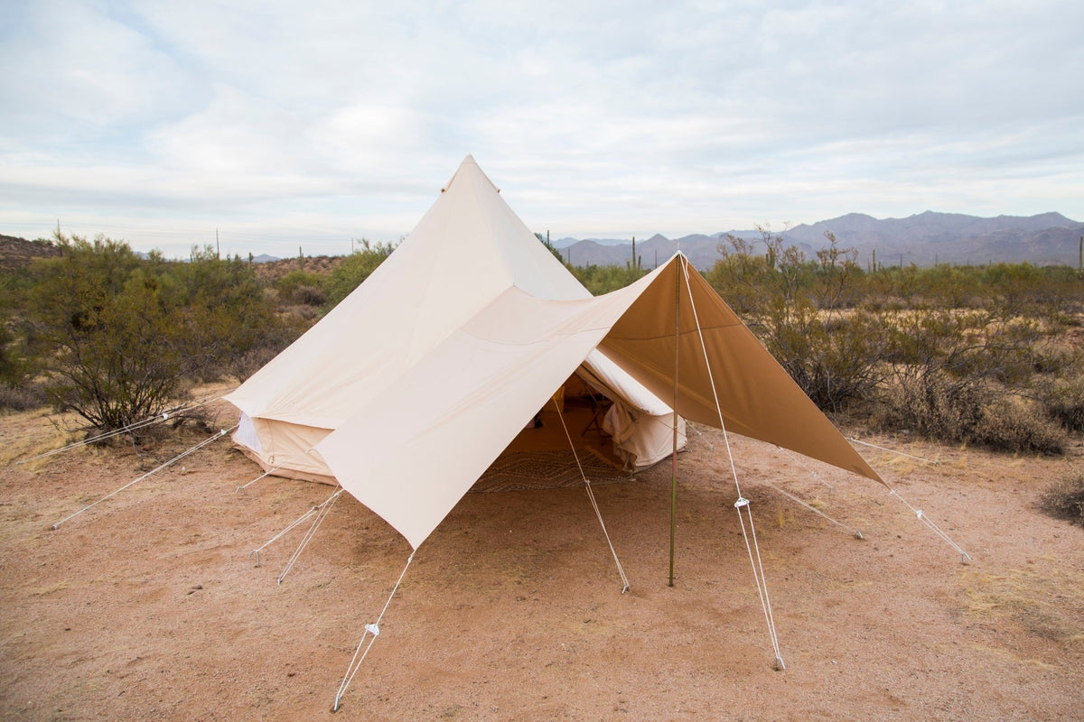 A tent with an awning set up in a desert landscape with mountains in the background.