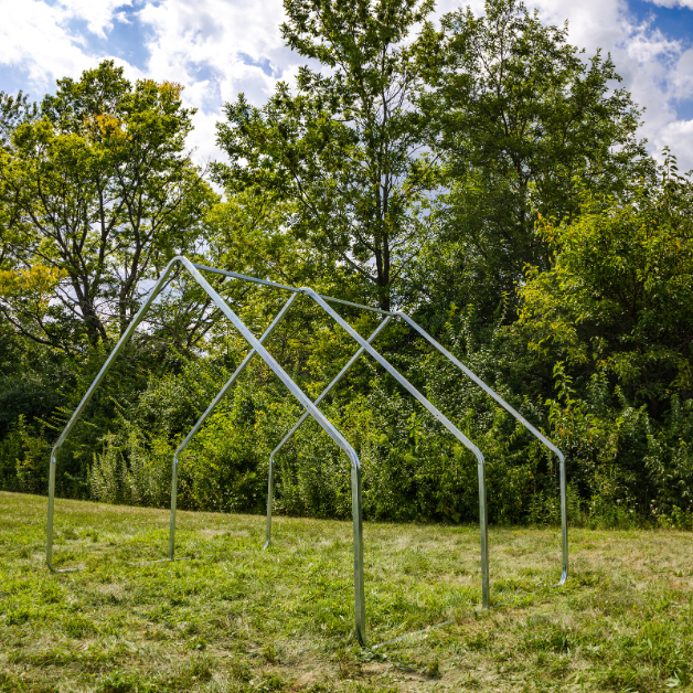 Metal tent frame structure on grass with trees in the background