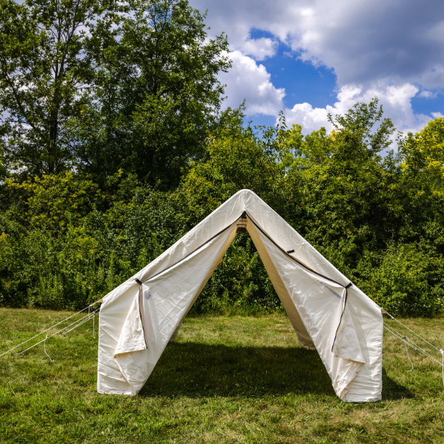 White wall tent set up in a grassy area with trees and blue sky in the background