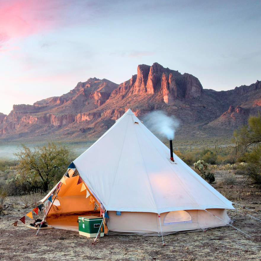Camping scene with a tent and stove in the desert at sunset.