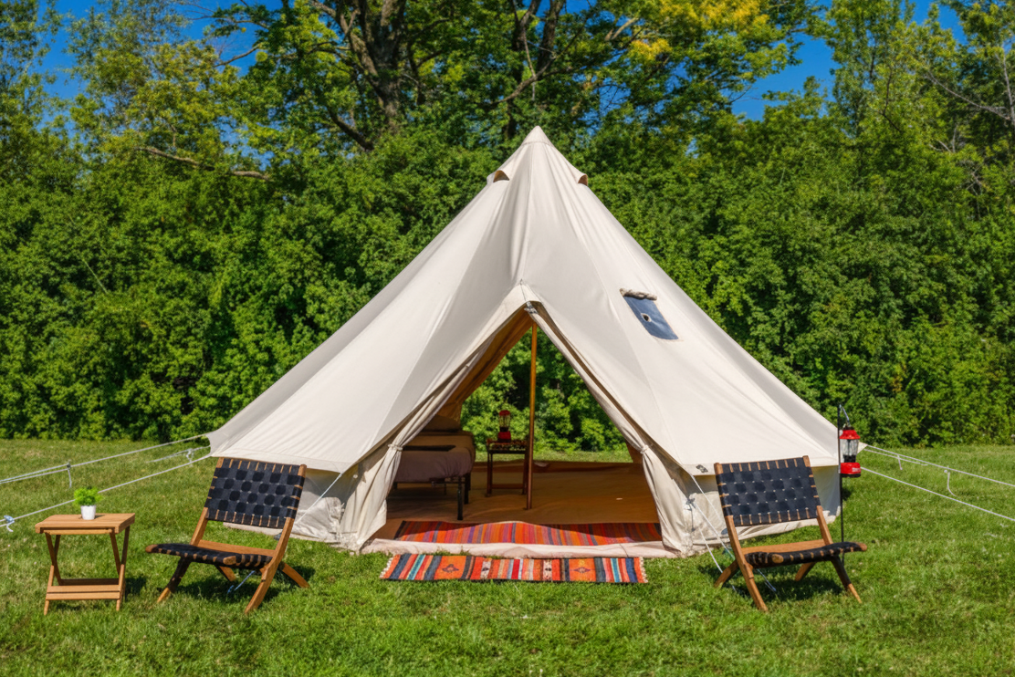 White bell tent with chairs and a table in a grassy area with trees