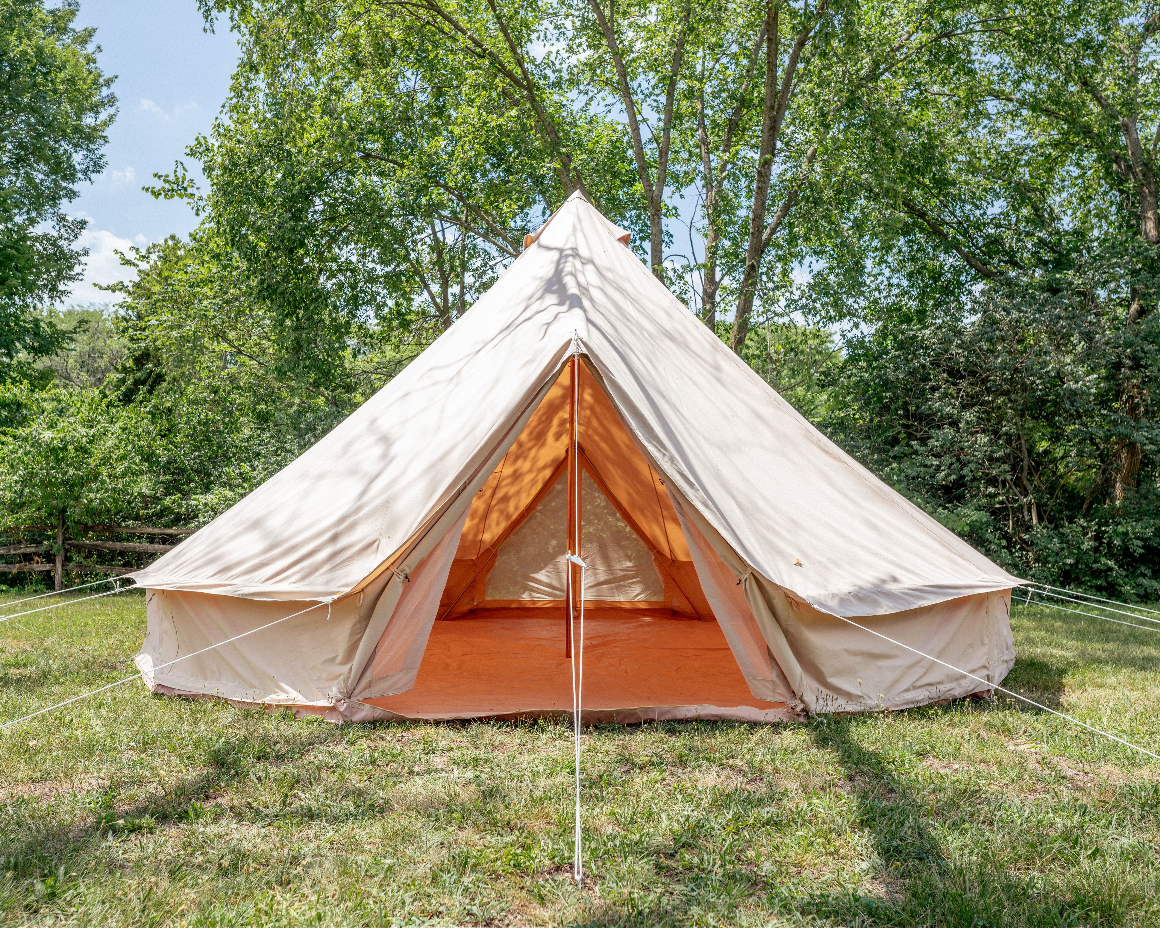 Beige bell tent with orange interior in a grassy area with trees