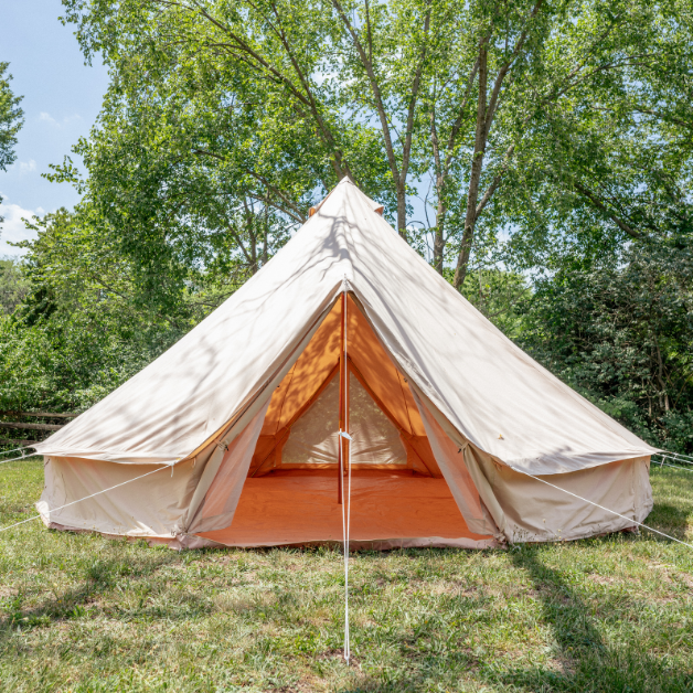 Beige bell tent with orange interior in a grassy area with trees