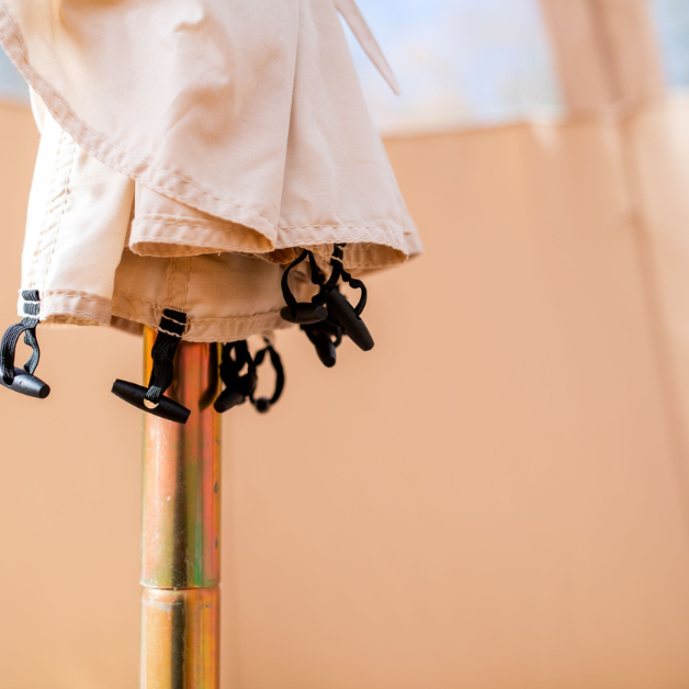 Close-up of a tent pole with beige fabric hanging with black toggles on the end