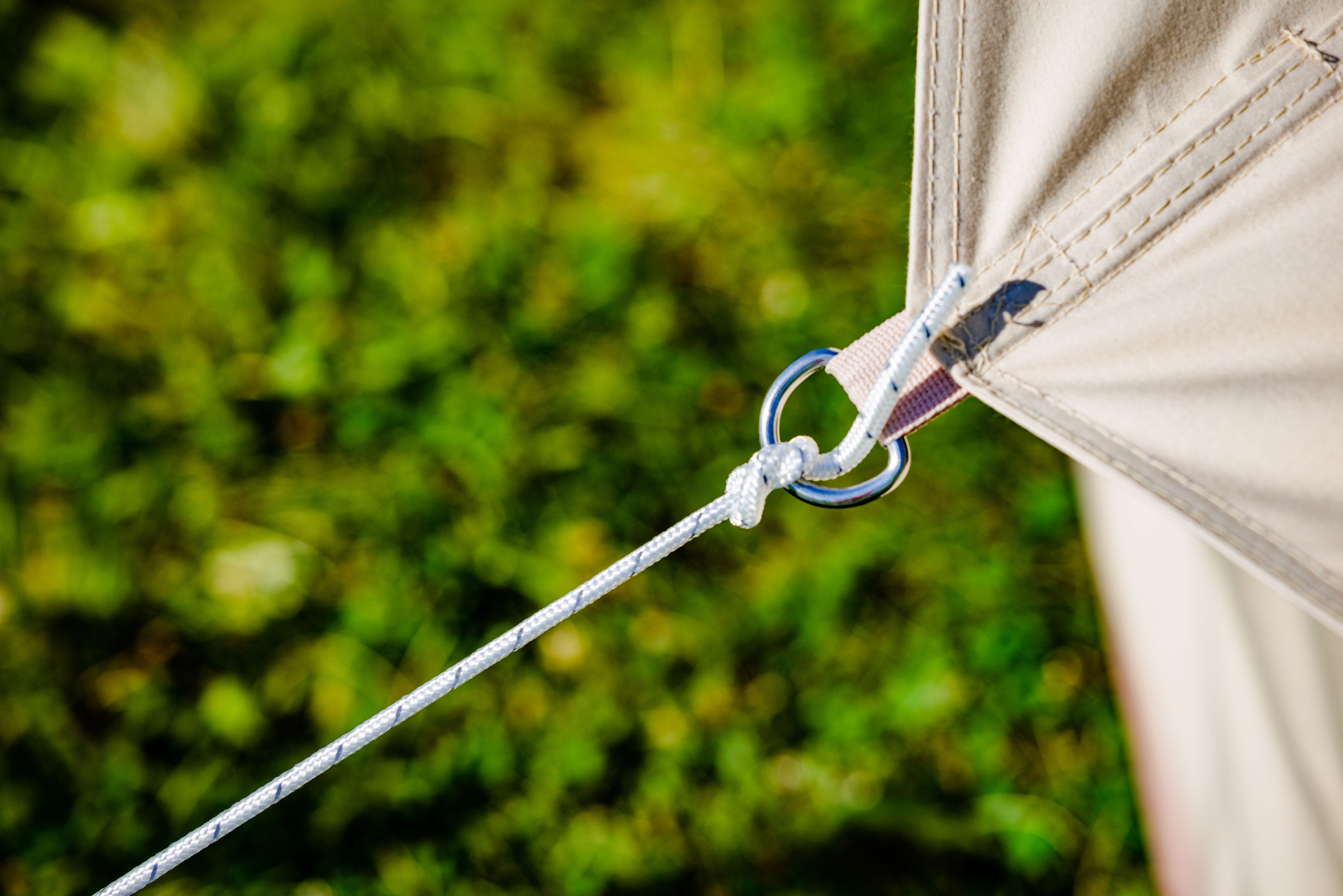 Close-up of a tent d-ring with a rope attached against a blurred green background