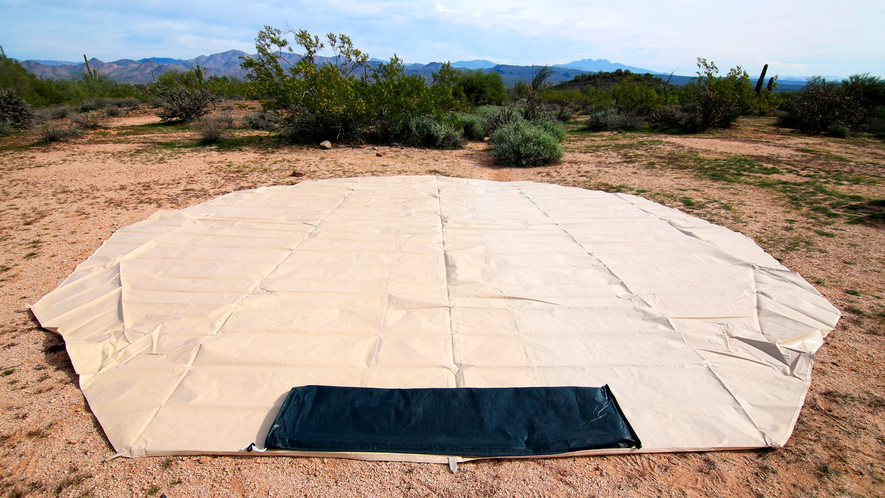 Large beige tent footpring on the ground with a rectangular black section in a desert landscape.
