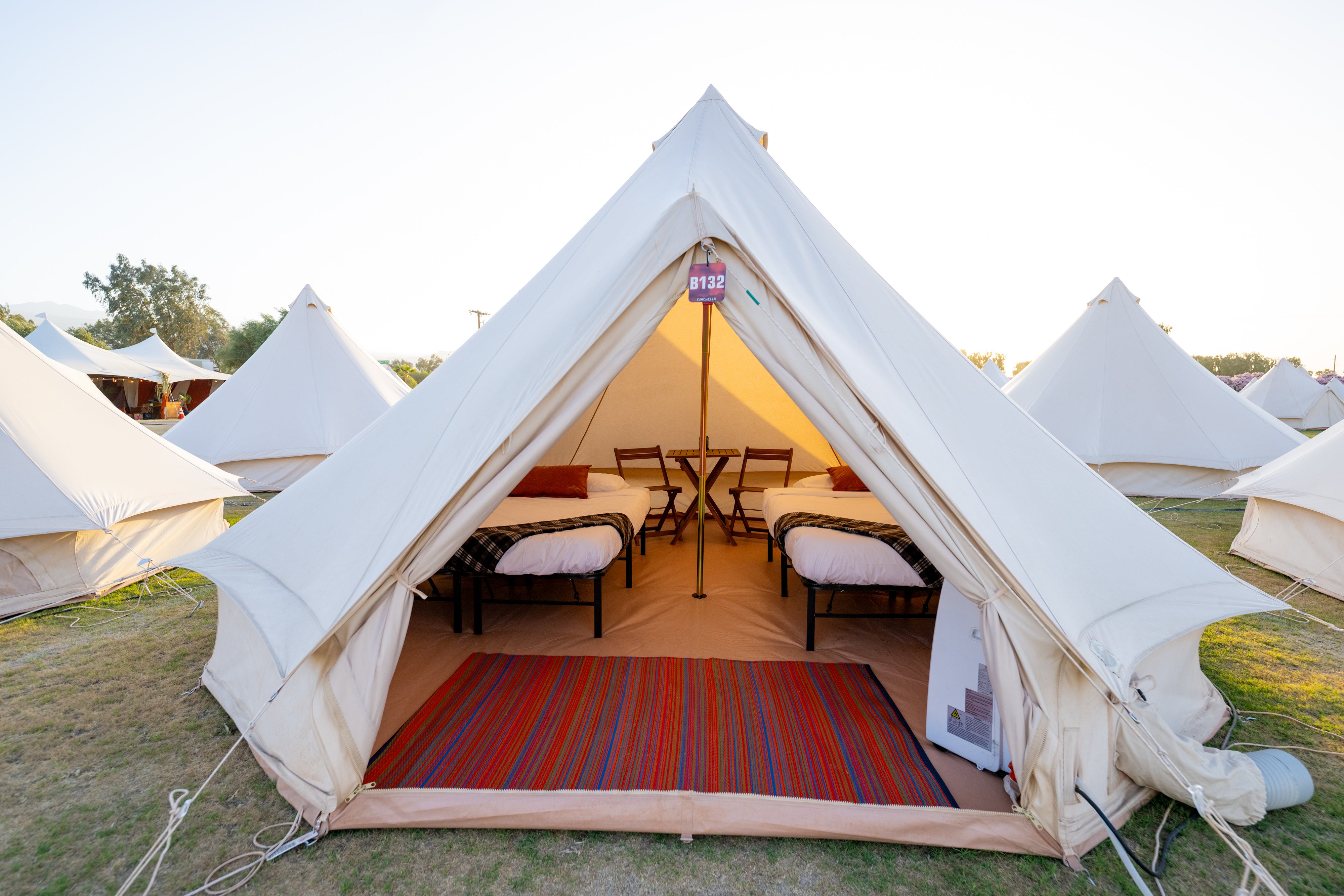 Large white tent with interior furniture and decor, surrounded by other tents in a field.