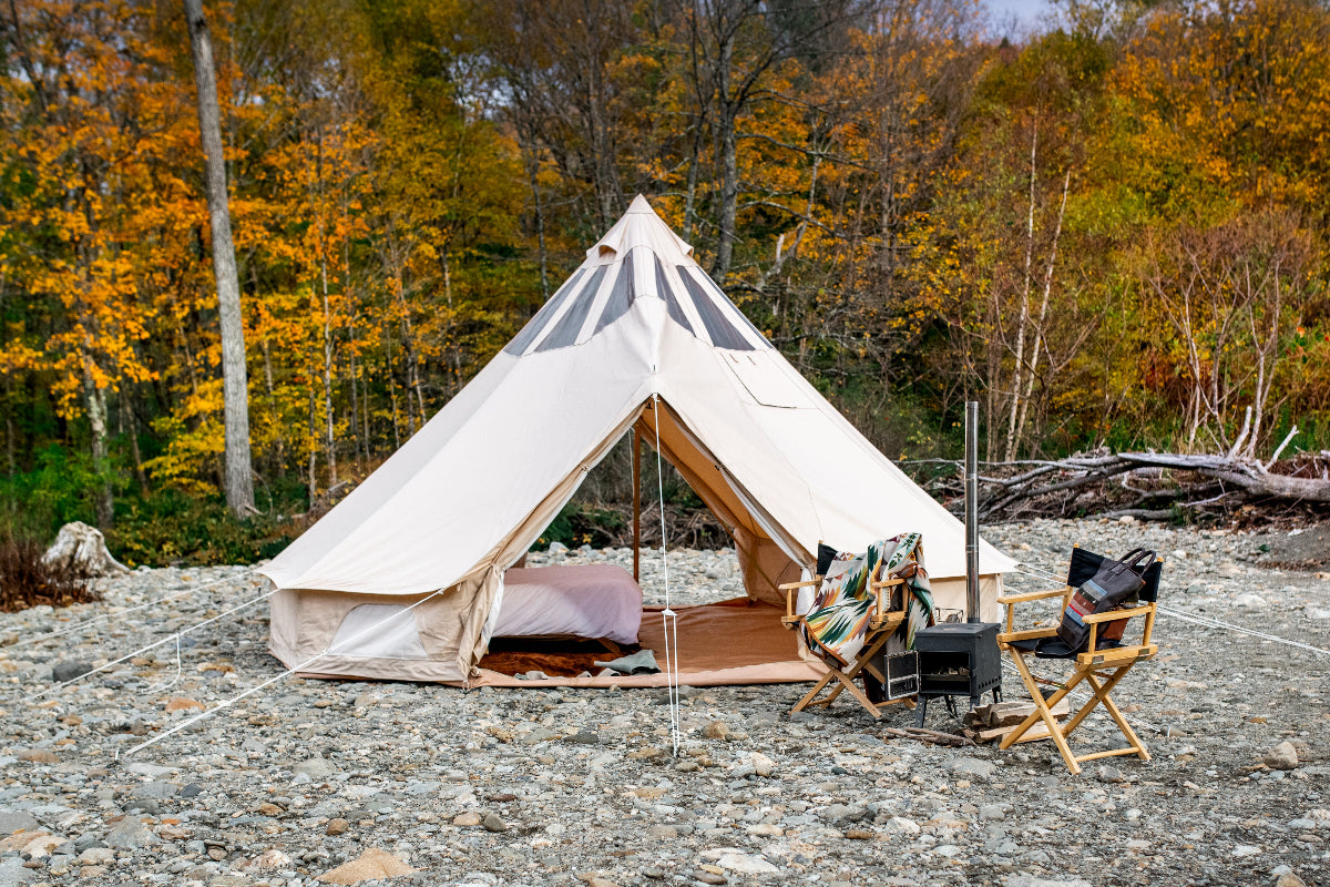 Beige bell tent in a forest setting with chairs and a fire pit.