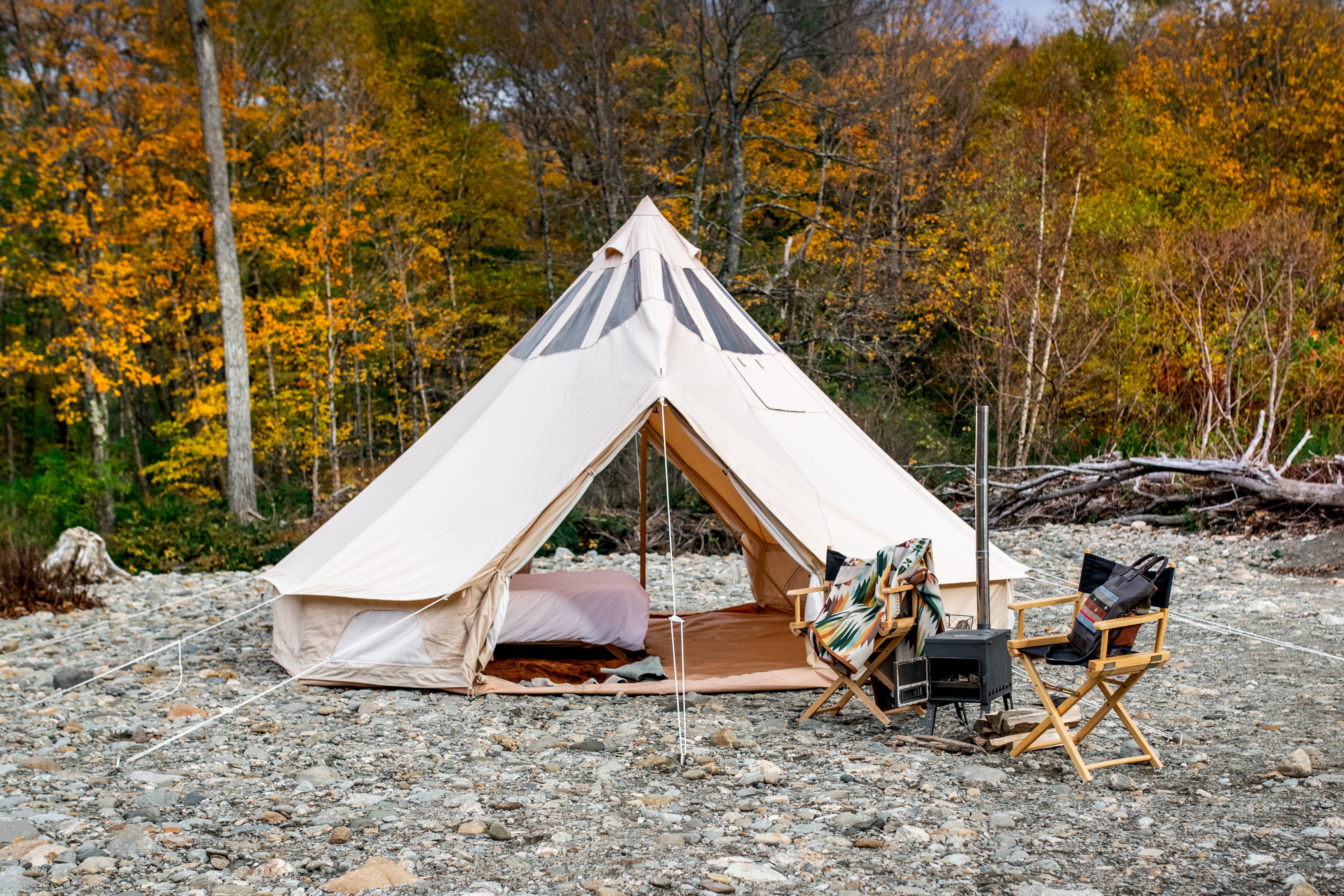 Beige bell tent in a forest setting with chairs and a fire pit.