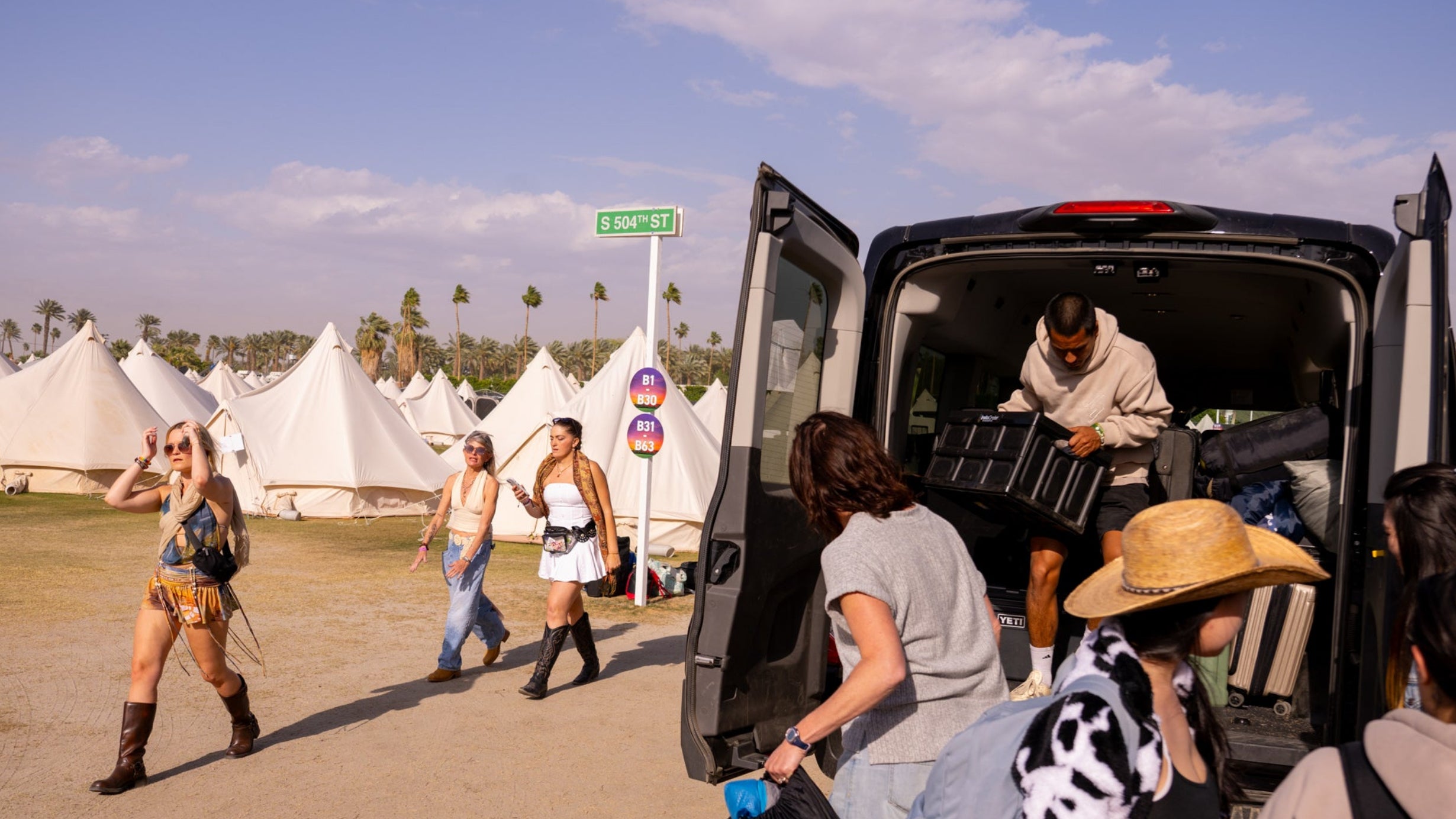 People at a festival with tents and a van in the background
