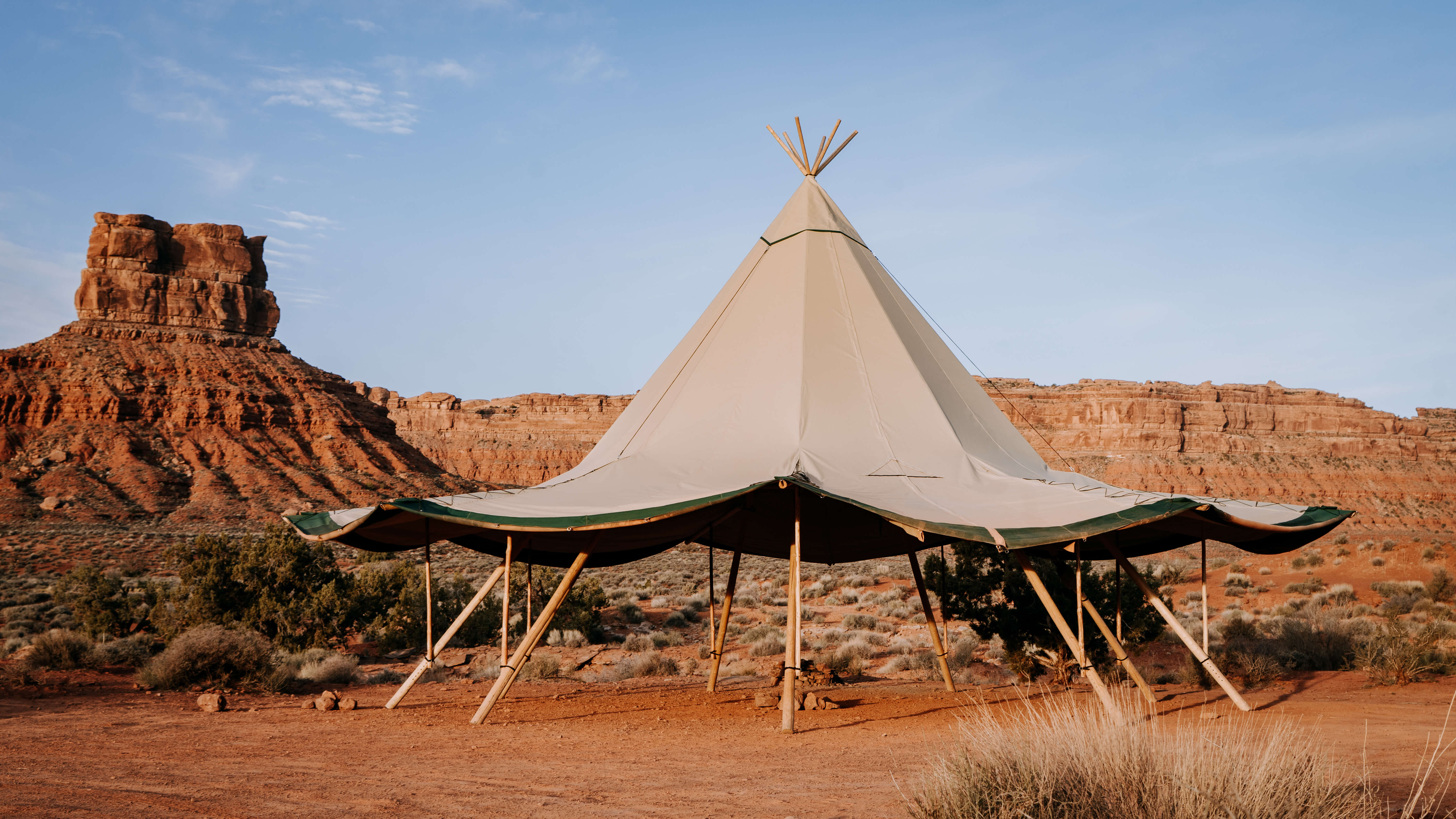 Tipi-style tent in a desert landscape with rocky formations and clear sky