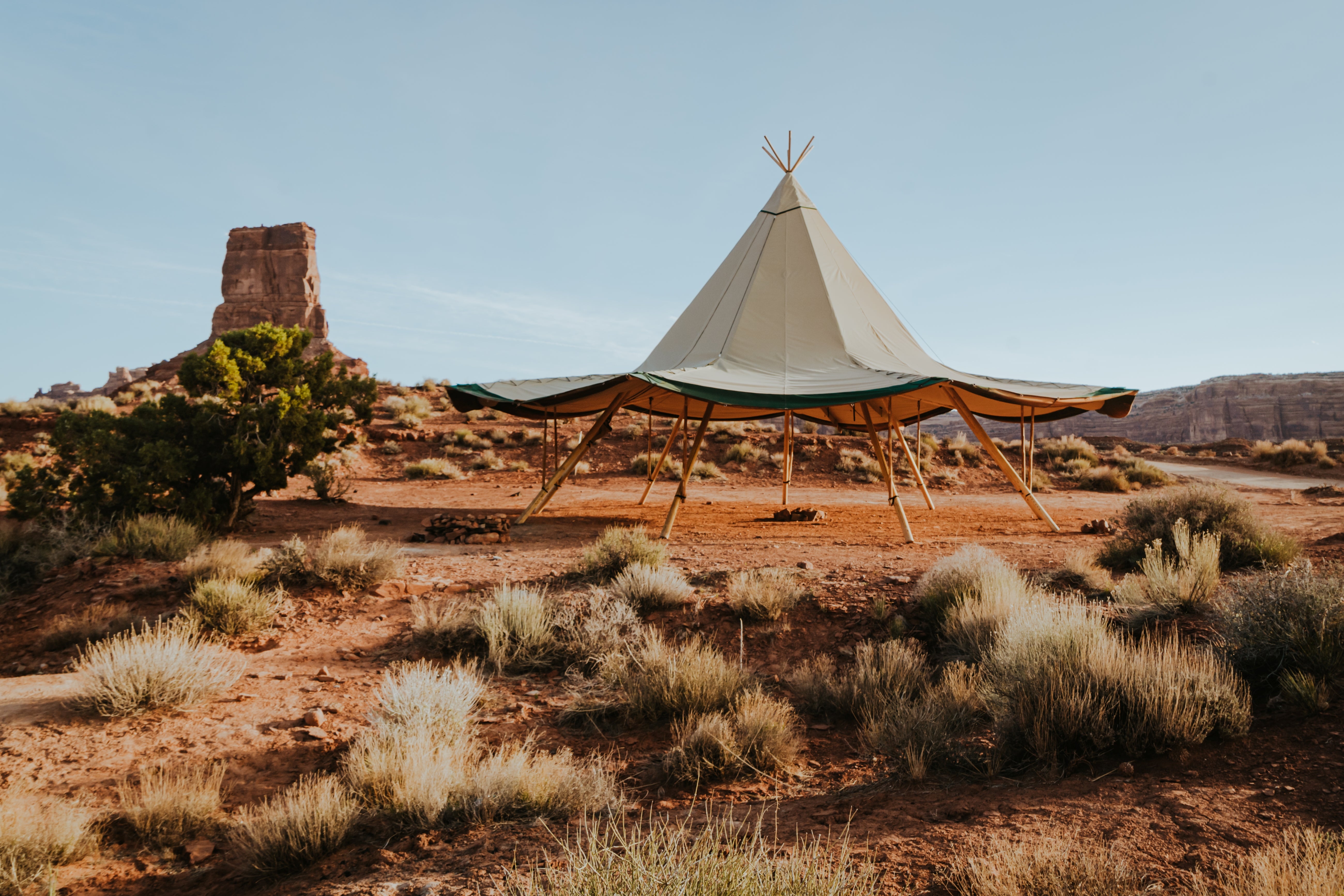 Teepee-style tent in a desert landscape with rocky formations and sparse vegetation.