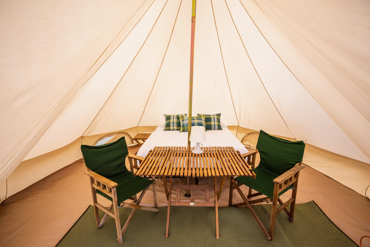 Interior of a tent with a wooden table and chairs, bed, and pillows.