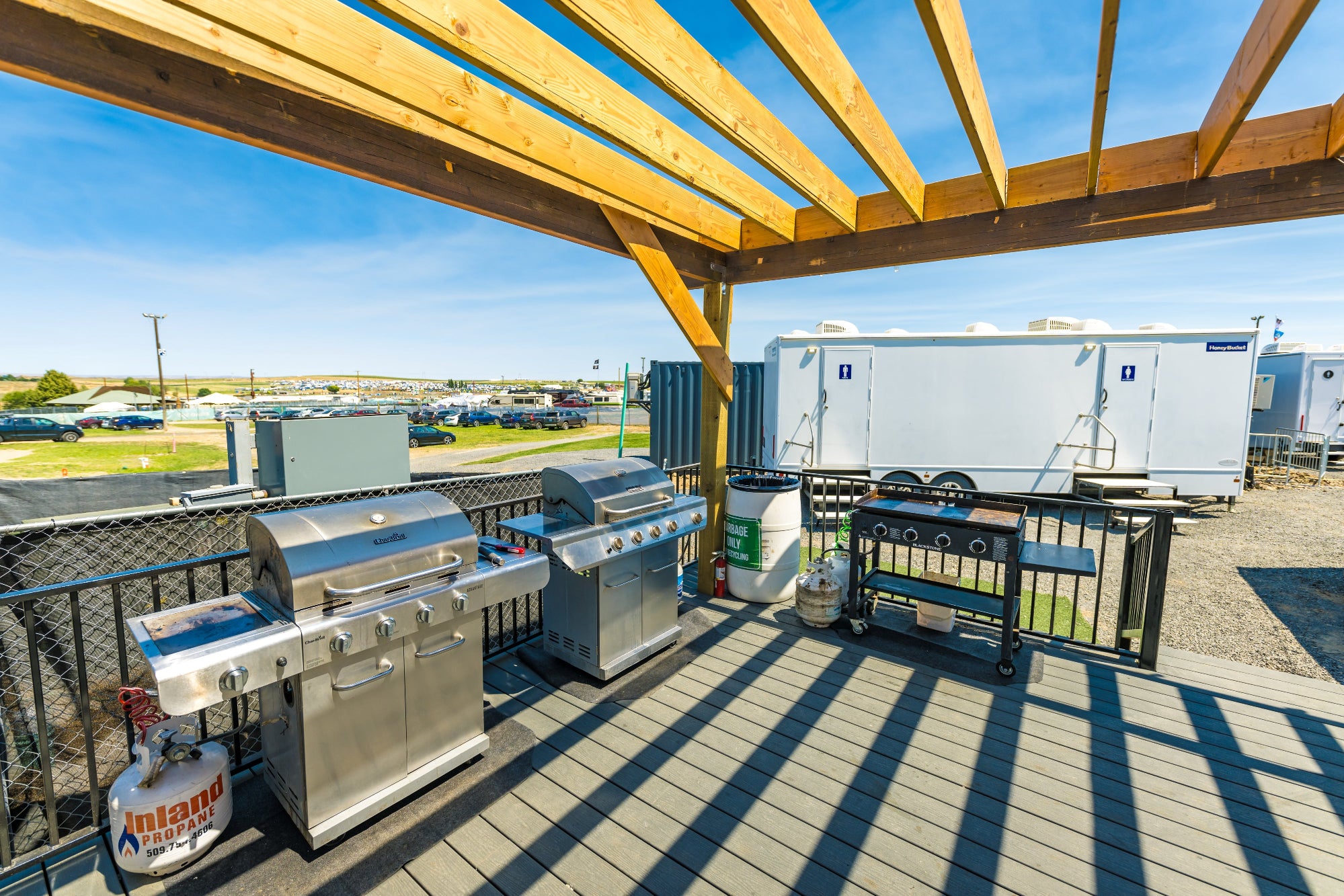 Outdoor grilling area with stainless steel grills under a wooden pergola.